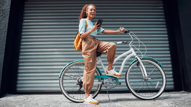 A woman is riding a bike while traveling and looking at the phone figuring out what should she do with her phone when traveling
