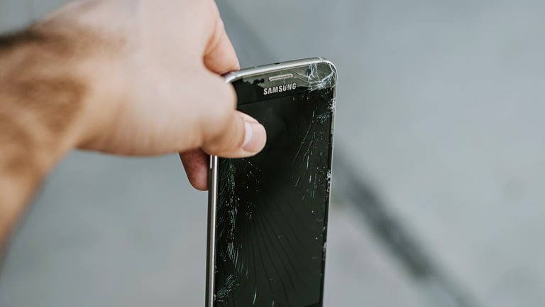 A hand holding damaged Samsung phone with damaged SIM card
